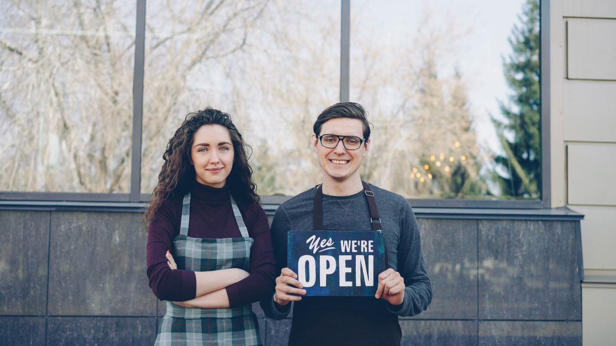 Small business owners holding an Open sign outside their local storefront